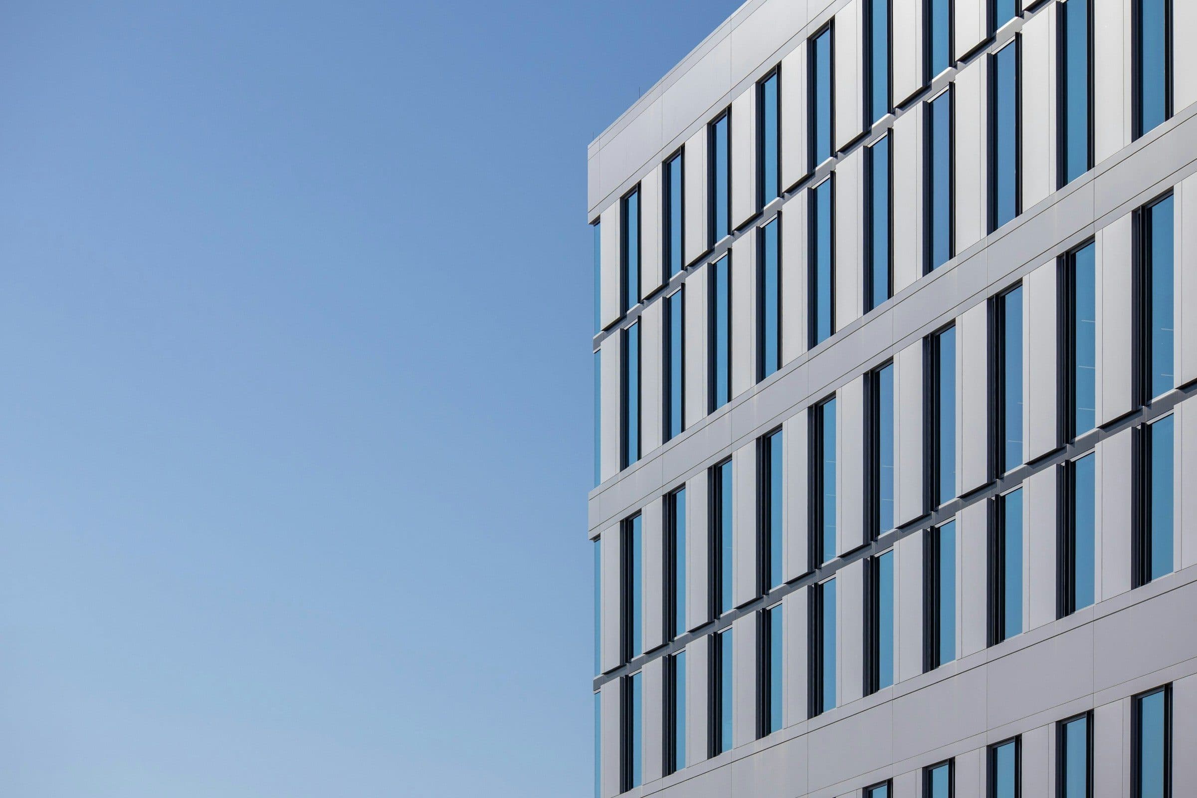 The edge of a white office facade with punched windows against a blue sky